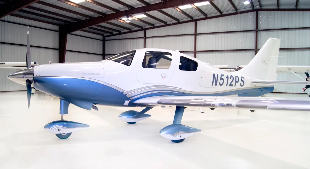 A white and blue Columbia 400 aircraft with registration N512PS is parked in a hangar, viewed from the front-right.