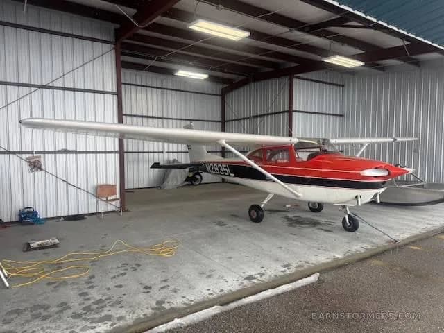 A red and white Cessna 172, registration N2835L, parked inside a metal hangar with a yellow extension cord on the floor.