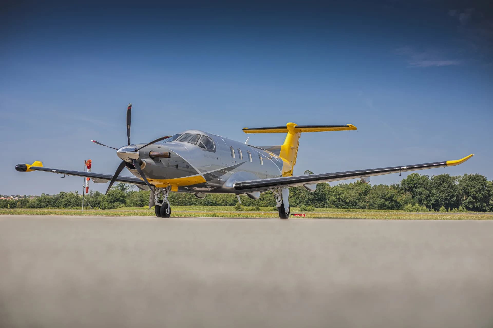 A front view of the silver and yellow Pilatus PC-12 aircraft (F-HPIL) parked on an airfield.