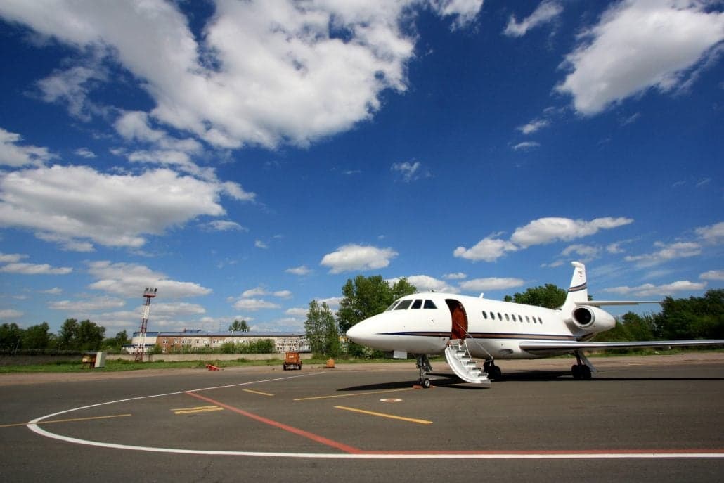A white private jet parked on the tarmac with the door open and stairs extended.