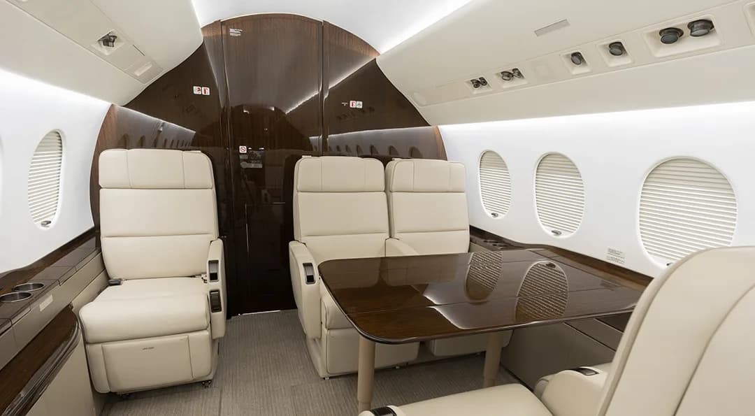 The aircraft interior features cream-colored leather seats and a wood table.