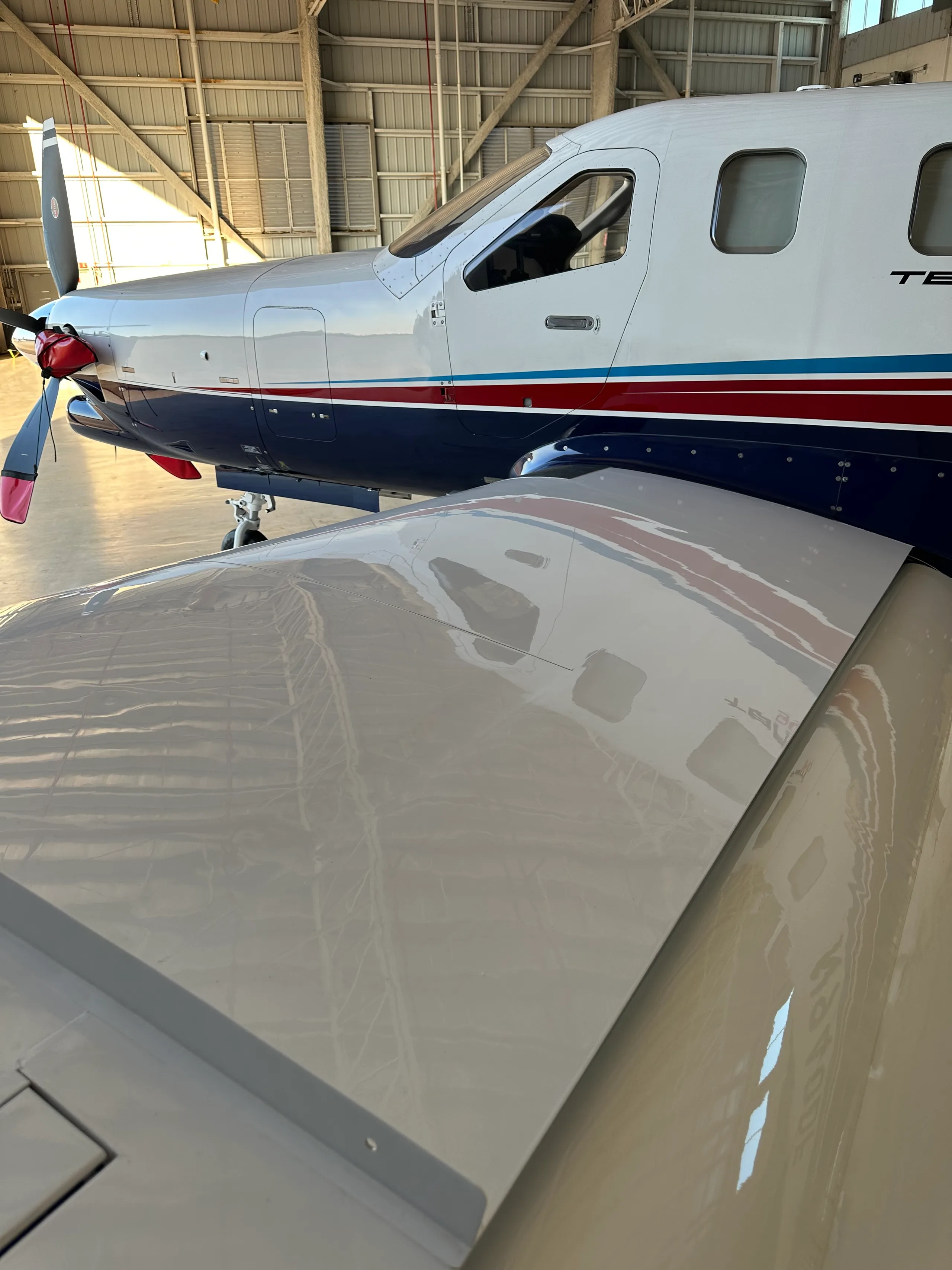 A close-up view of the wing and fuselage of a TBM 940 aircraft inside a hangar.