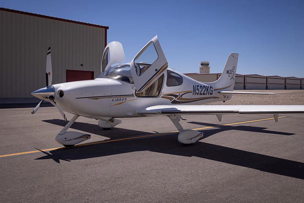 A white Cirrus SR22 aircraft with gold and black stripes, registration N522KG, parked on an airfield with its doors open.