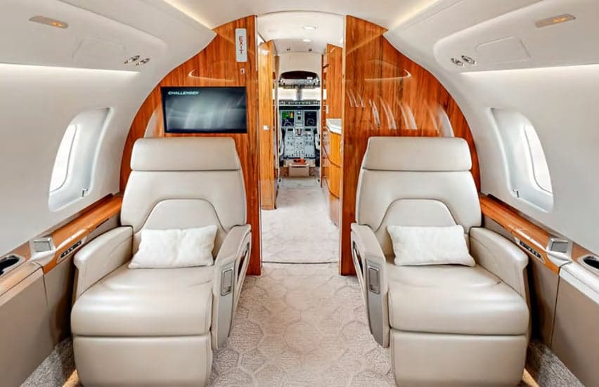 The aircraft's interior features leather seats and wood trim with a view towards the cockpit.