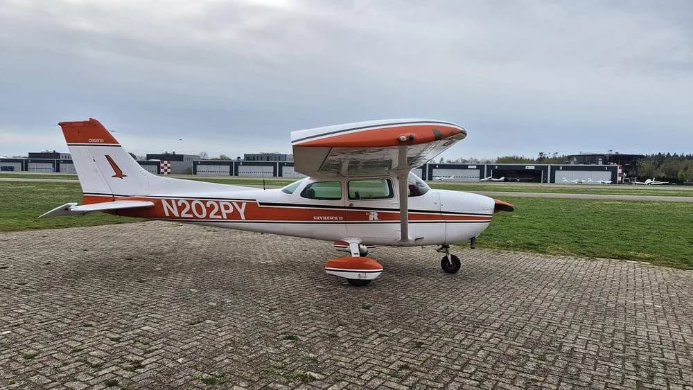 A white and orange Cessna Skyhawk II N202PY parked on a paved apron at an airfield.