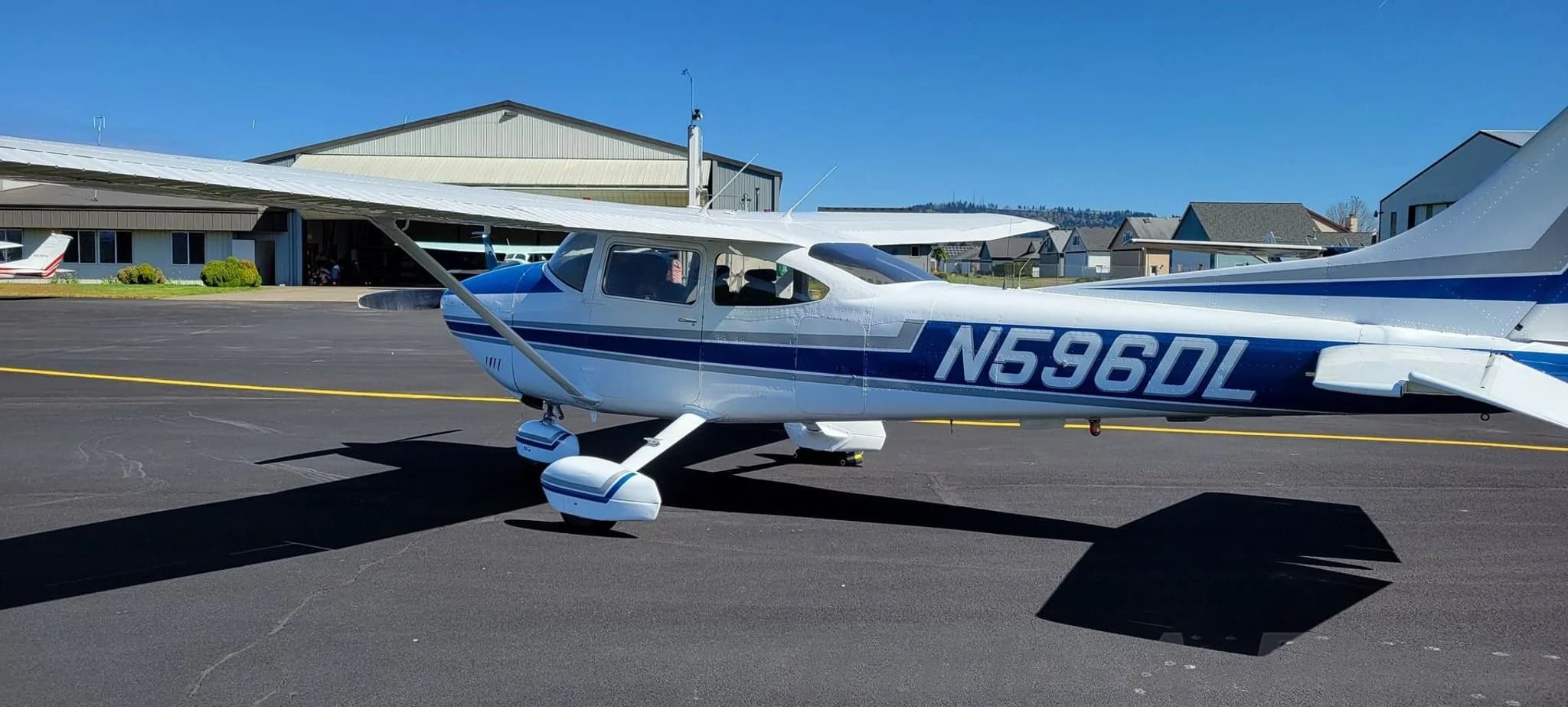 A white and blue Cessna 182 Skylane aircraft with registration N596DL parked on an airfield.