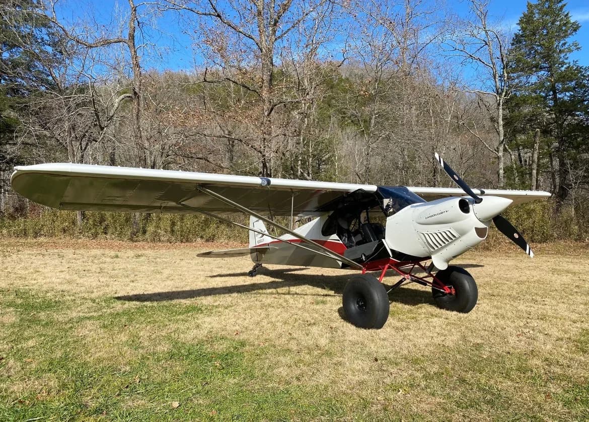 A white and red Carbon Cub aircraft on a grassy field.