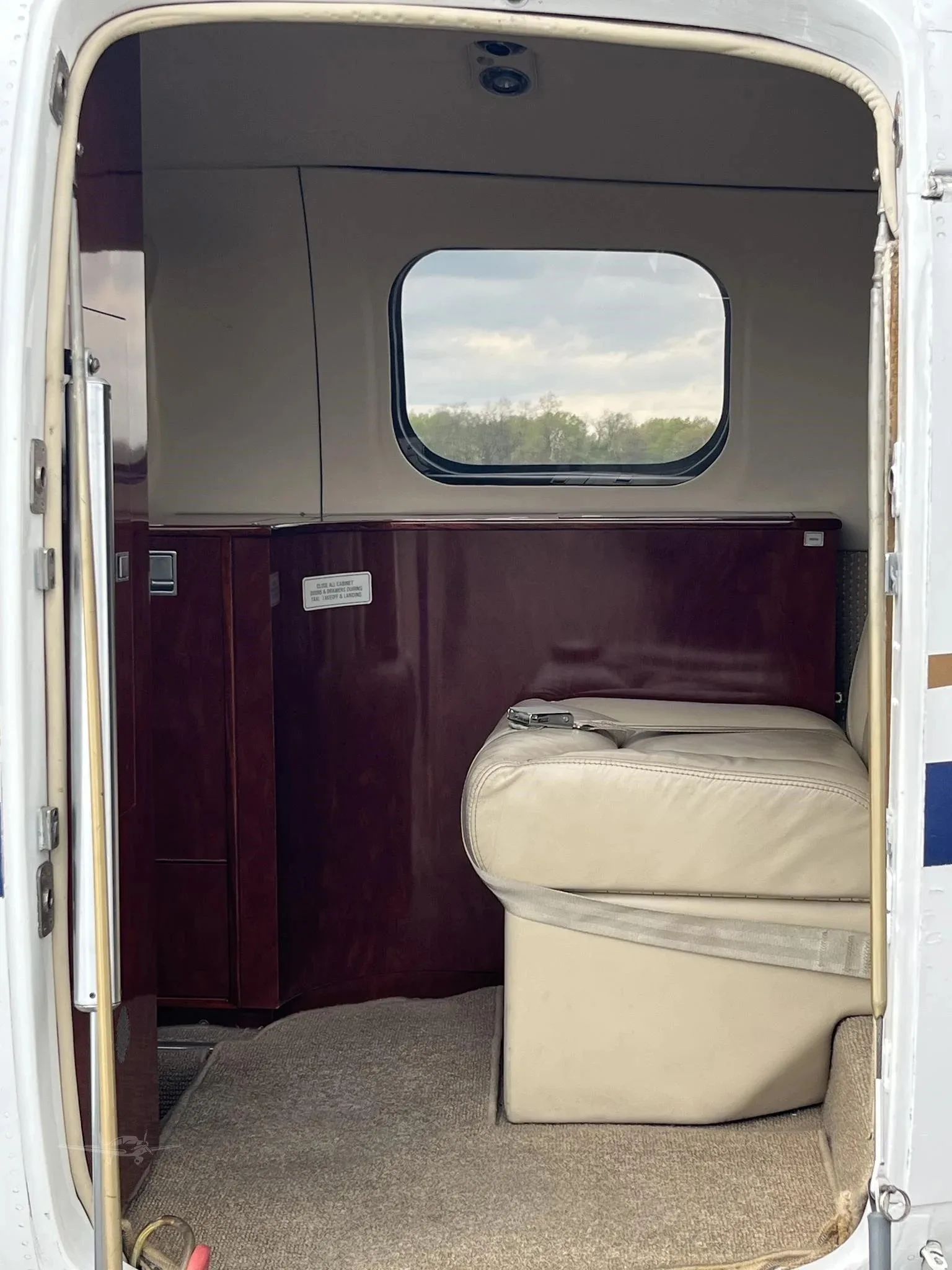View from the open door into the aircraft cabin, showing a beige leather seat and dark wood paneling.