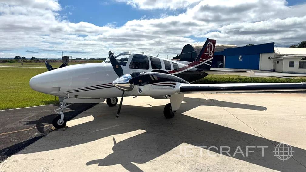 A Beechcraft Baron aircraft is parked on the tarmac on a sunny day.