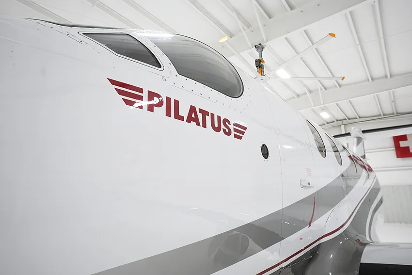 A close-up view of the cockpit windows and "PILATUS" logo on the side of a white Pilatus PC-12 aircraft.