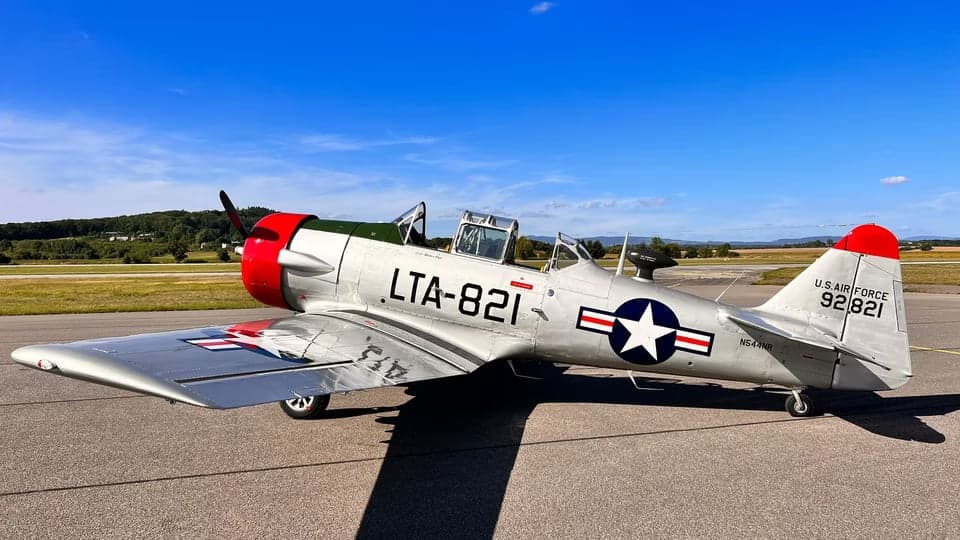 A T-6 Texan aircraft in flight with a silver and red paint scheme.