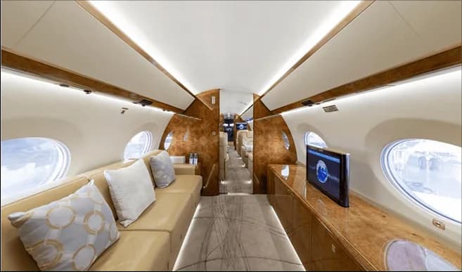 A wide view of the private jet's interior cabin, featuring a long sofa and a television screen.