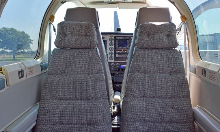 The aircraft's cabin interior shows two rows of grey patterned seats looking towards the cockpit.