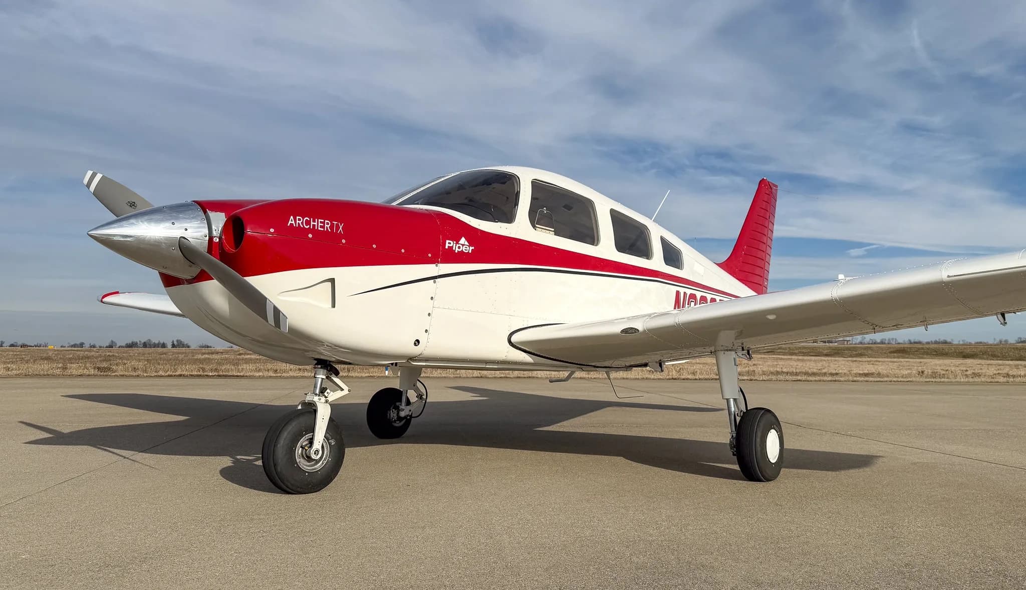 A close-up, low-angle view of the front-left side of a white and red Piper Archer TX, N232TF, on an airfield.