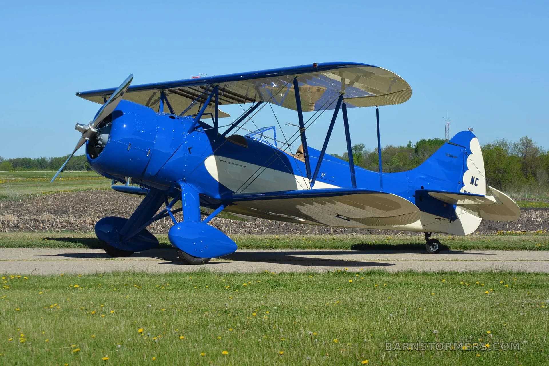 A blue and white biplane with registration N32063 parked on an asphalt runway next to a grassy field.