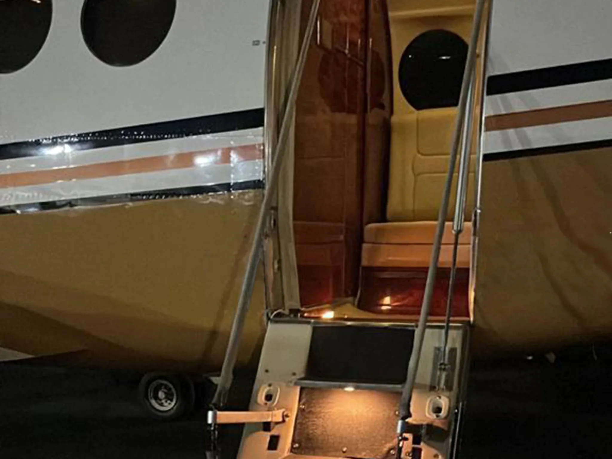 A close-up view of the illuminated open airstairs and entry of a white and gold turboprop aircraft.