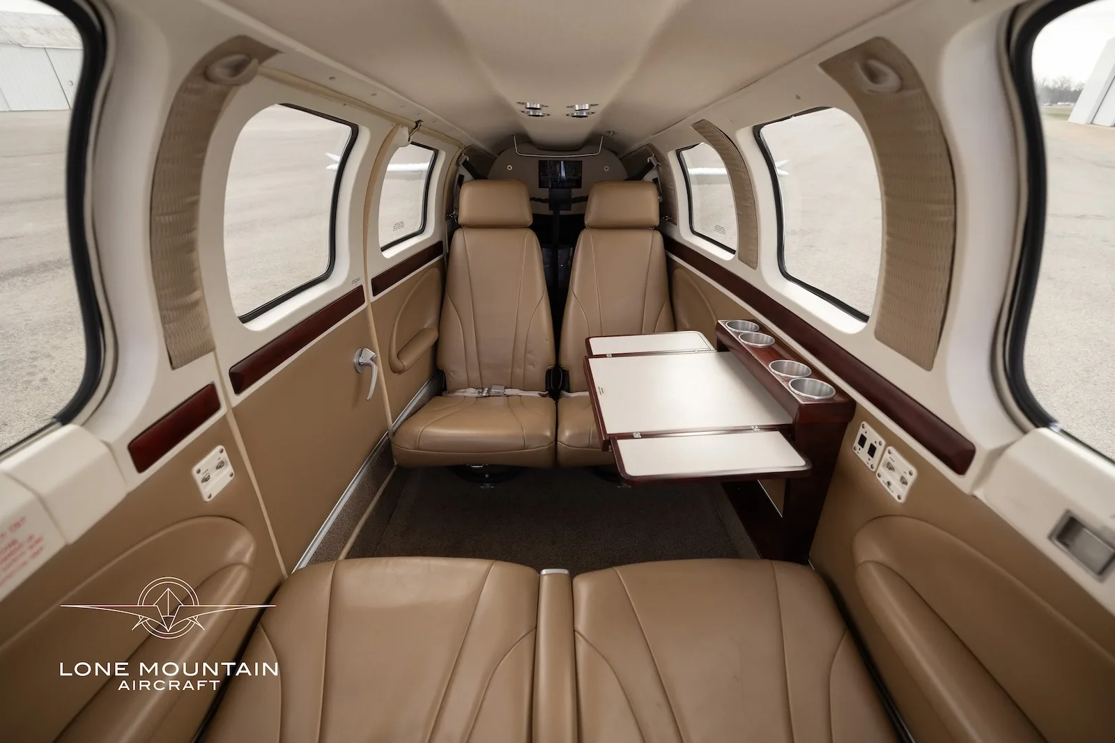 The aircraft's cabin interior features tan leather seats, a fold-out table with cup holders, and large windows.