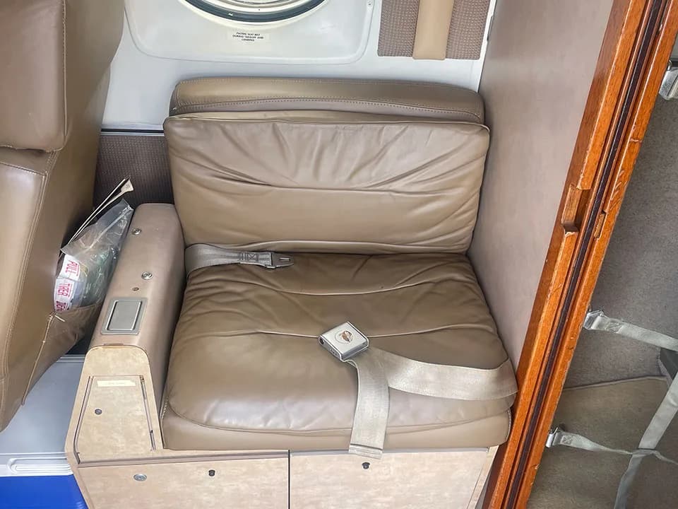 A close-up of a tan leather passenger seat with an armrest and seatbelt in the aircraft cabin.