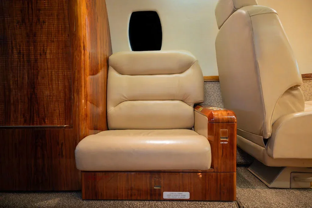 A close-up of a beige leather cabin seat with a wooden armrest and surrounding wood paneling.