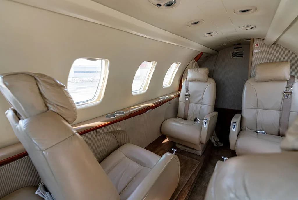 A side view of the private jet's interior cabin, featuring beige leather seats and multiple windows.