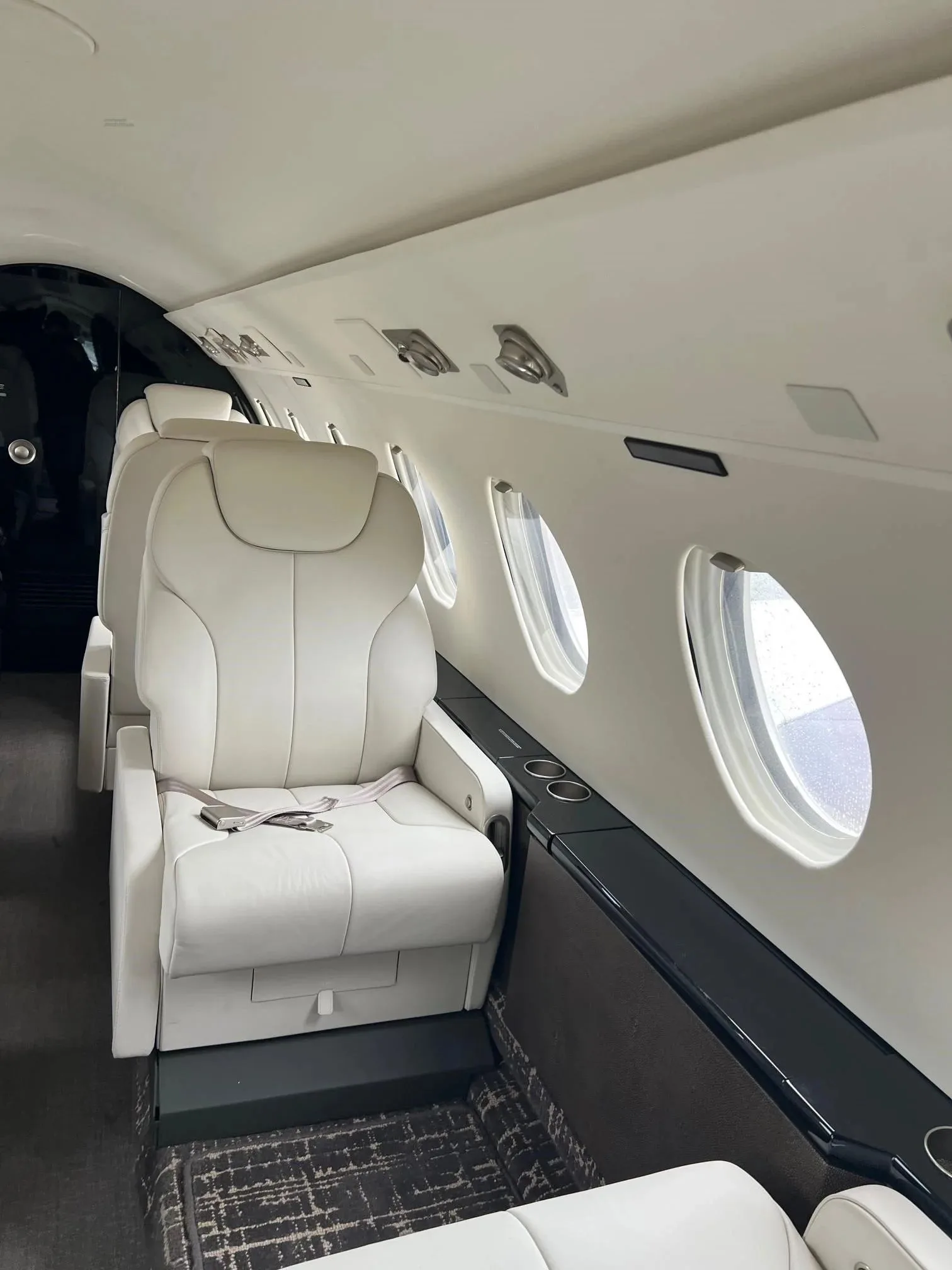 A view down the cabin of a business jet, showing several white leather seats and windows.