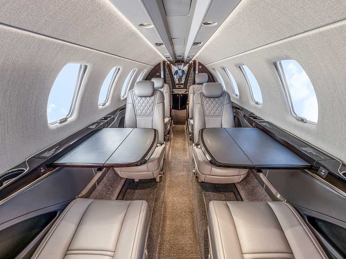 View of the Citation CJ4 cabin featuring gray leather seats, light-colored carpet, and fold-down tables.