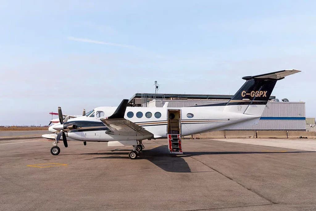 A side view of a white and black twin-engine turboprop aircraft (King Air) with tail number C-GGPX, showing the passenger door open with stairs.