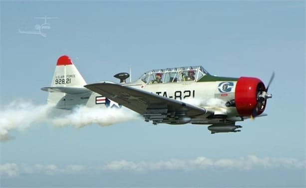 A T-6 Texan aircraft in flight with a silver and red paint scheme.