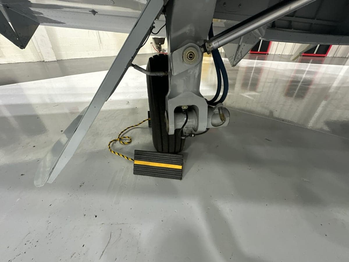 Close up of the aircraft's nose wheel and strut in a hangar setting.