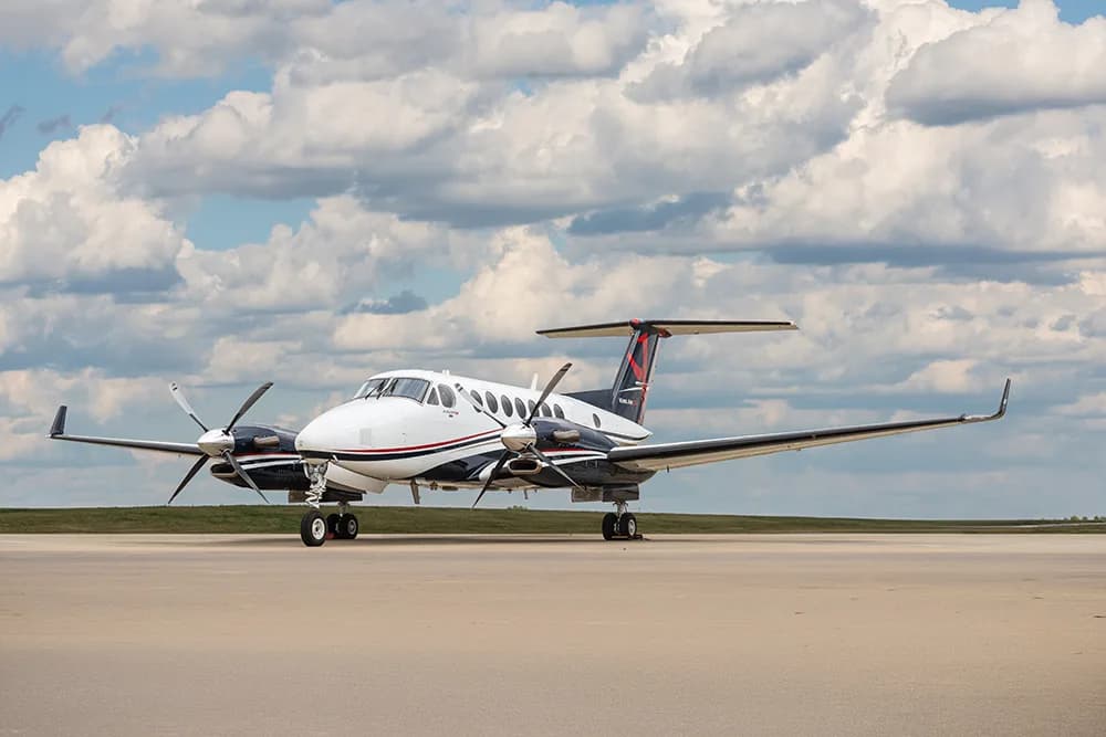 A white and black Beechcraft King Air 350 turboprop aircraft parked on a tarmac under a cloudy sky.