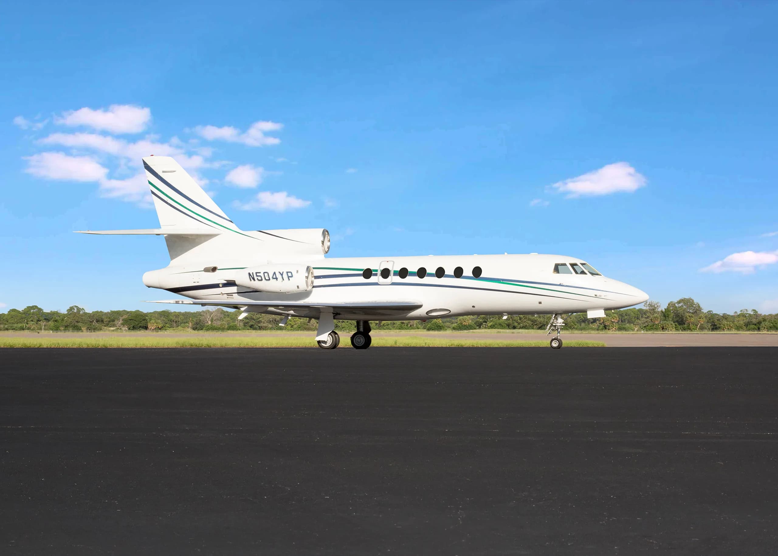 A white business jet with green and blue stripes and registration N504YP parked on a tarmac under a blue sky.