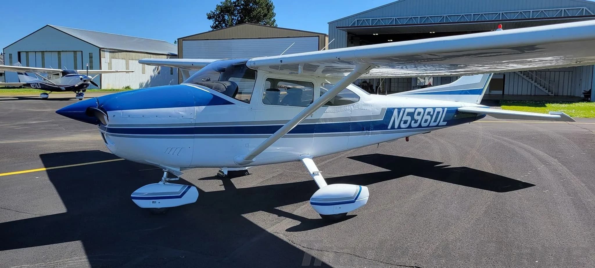 Front-side view of a white and blue Cessna 182 Skylane aircraft with registration N596DL on an airfield.
