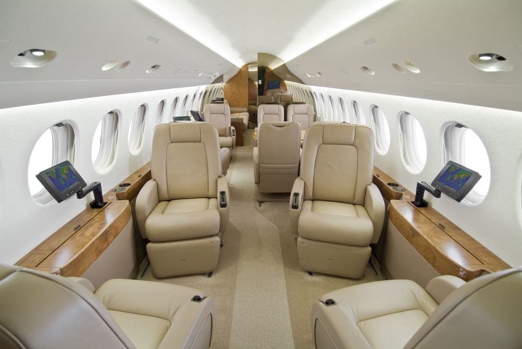 The interior of a private jet with beige leather seats and wood trim.
