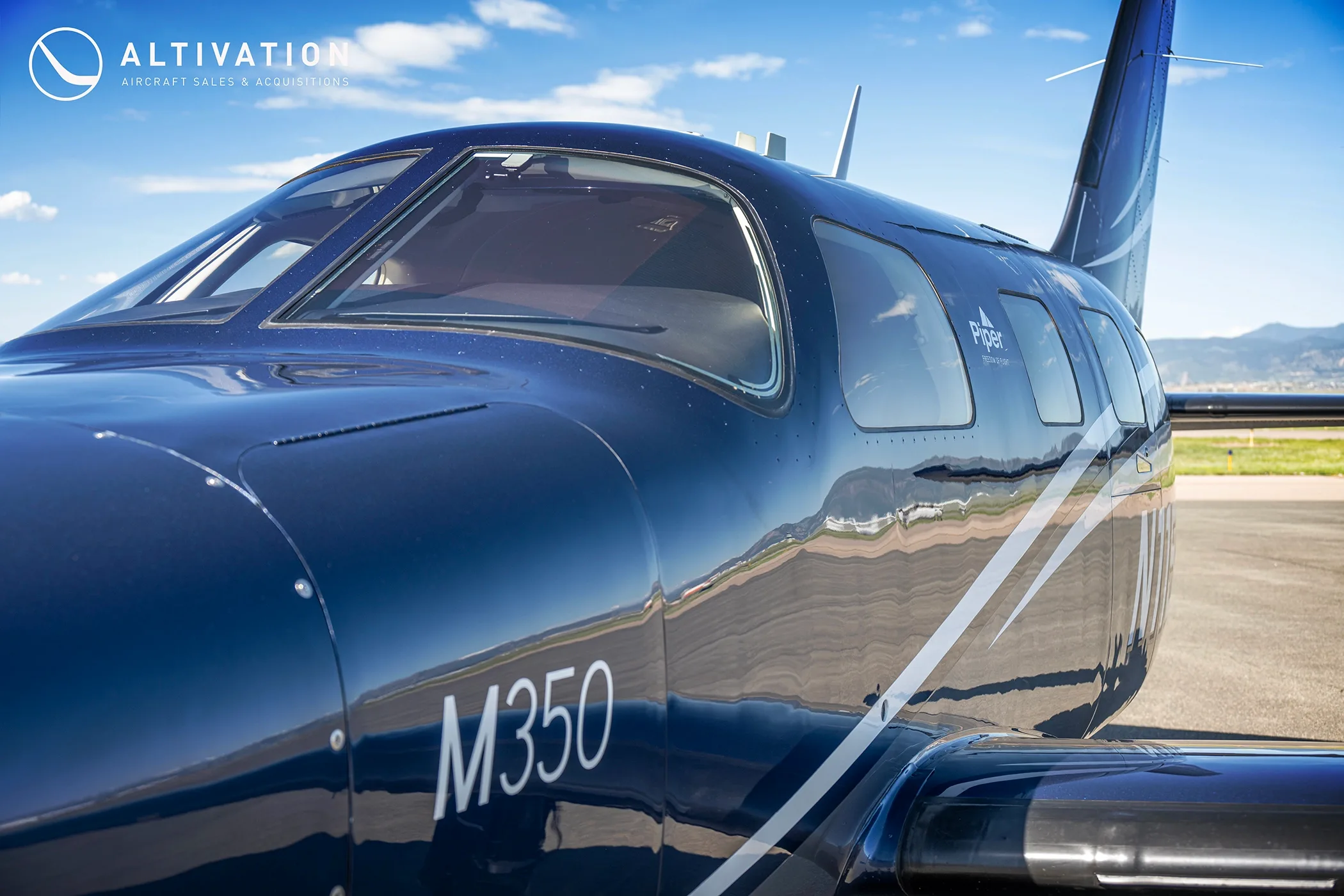 A close-up view of the cockpit and front fuselage of the dark blue Piper M350.