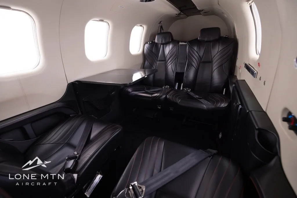 A view of the black leather passenger seats and a side table in the cabin of a TBM 940 aircraft.