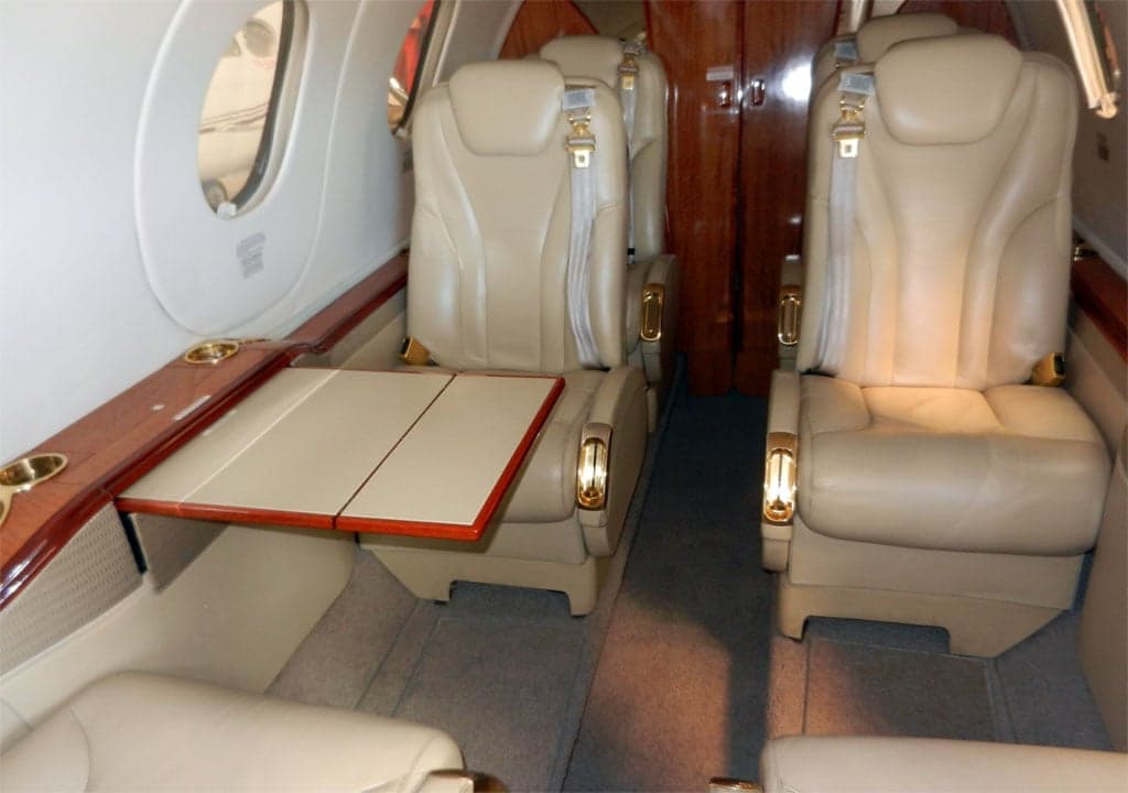 Interior view of the jet cabin with tan leather seats, wood trim, and a fold-out table.