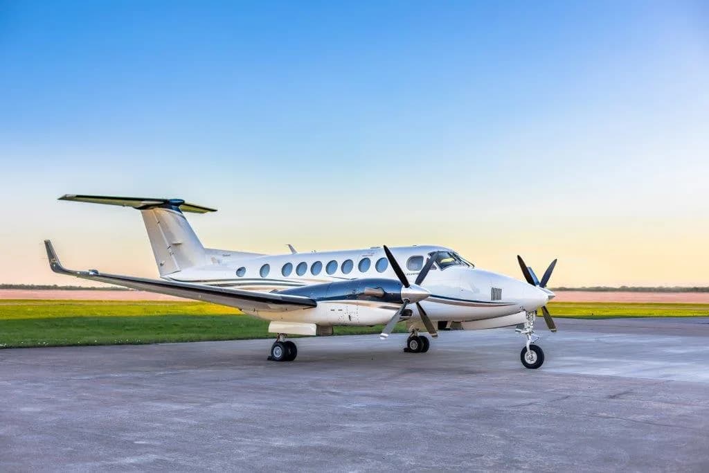 A white and black Beechcraft King Air 350i turboprop aircraft parked on an airfield at sunset.