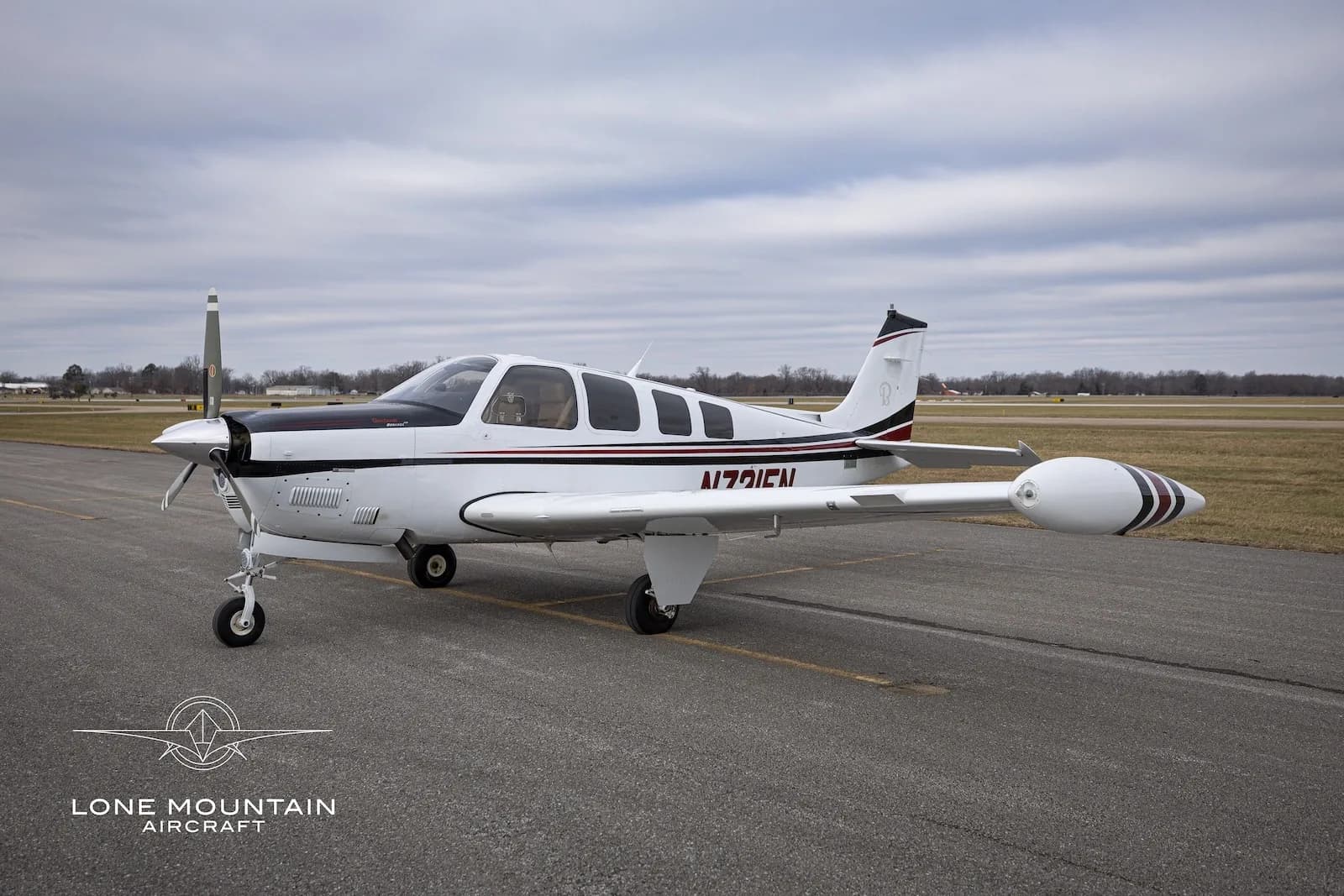 A white and black single-engine propeller aircraft with red stripes, N721EN, parked on an asphalt runway under a cloudy sky.
