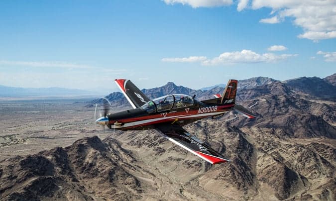 A Beechcraft T-6C Texan II aircraft in flight over a desert landscape.