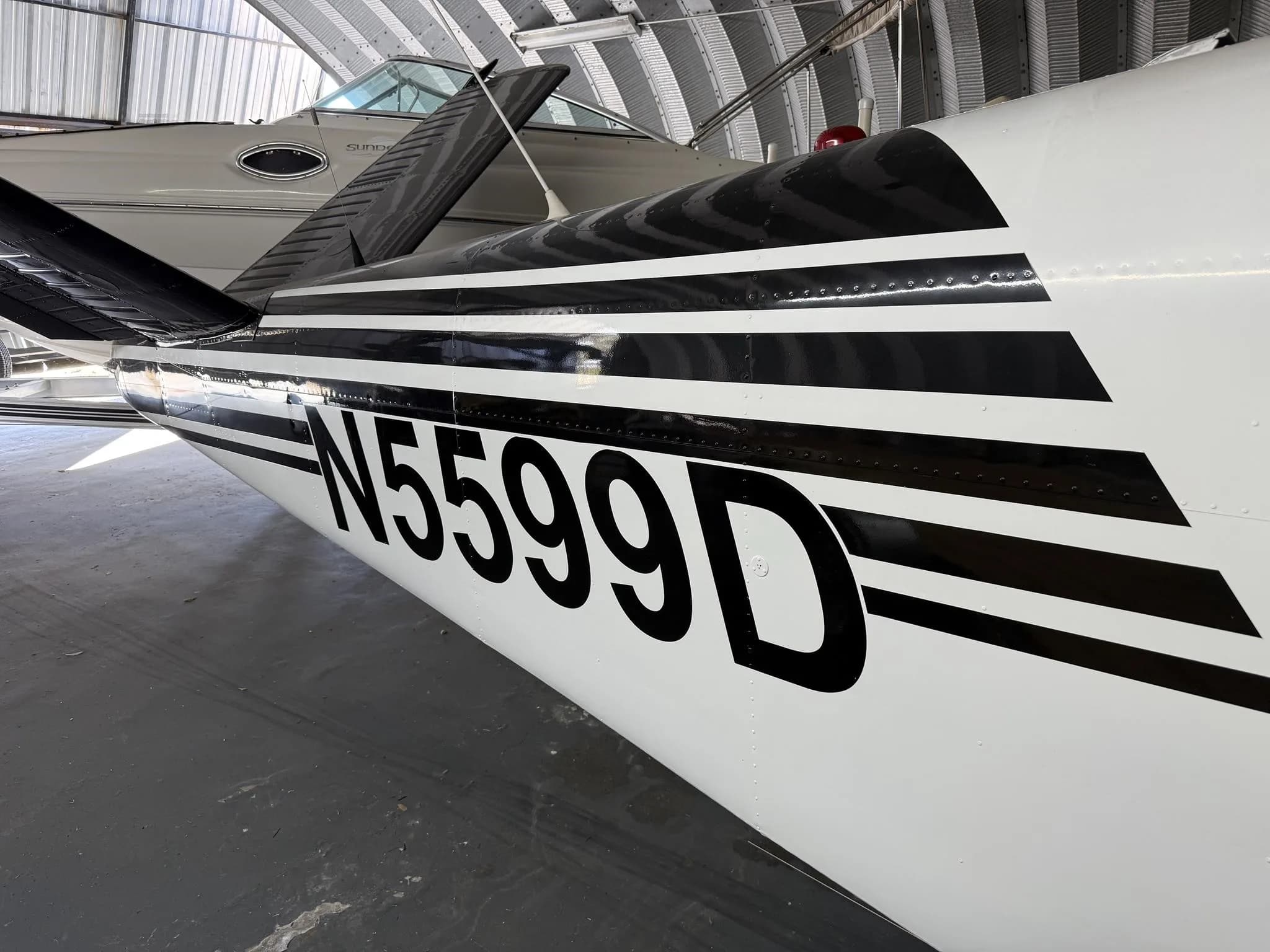 A close-up of the tail section of a white aircraft with black stripes and N5599D registration, in a hangar.