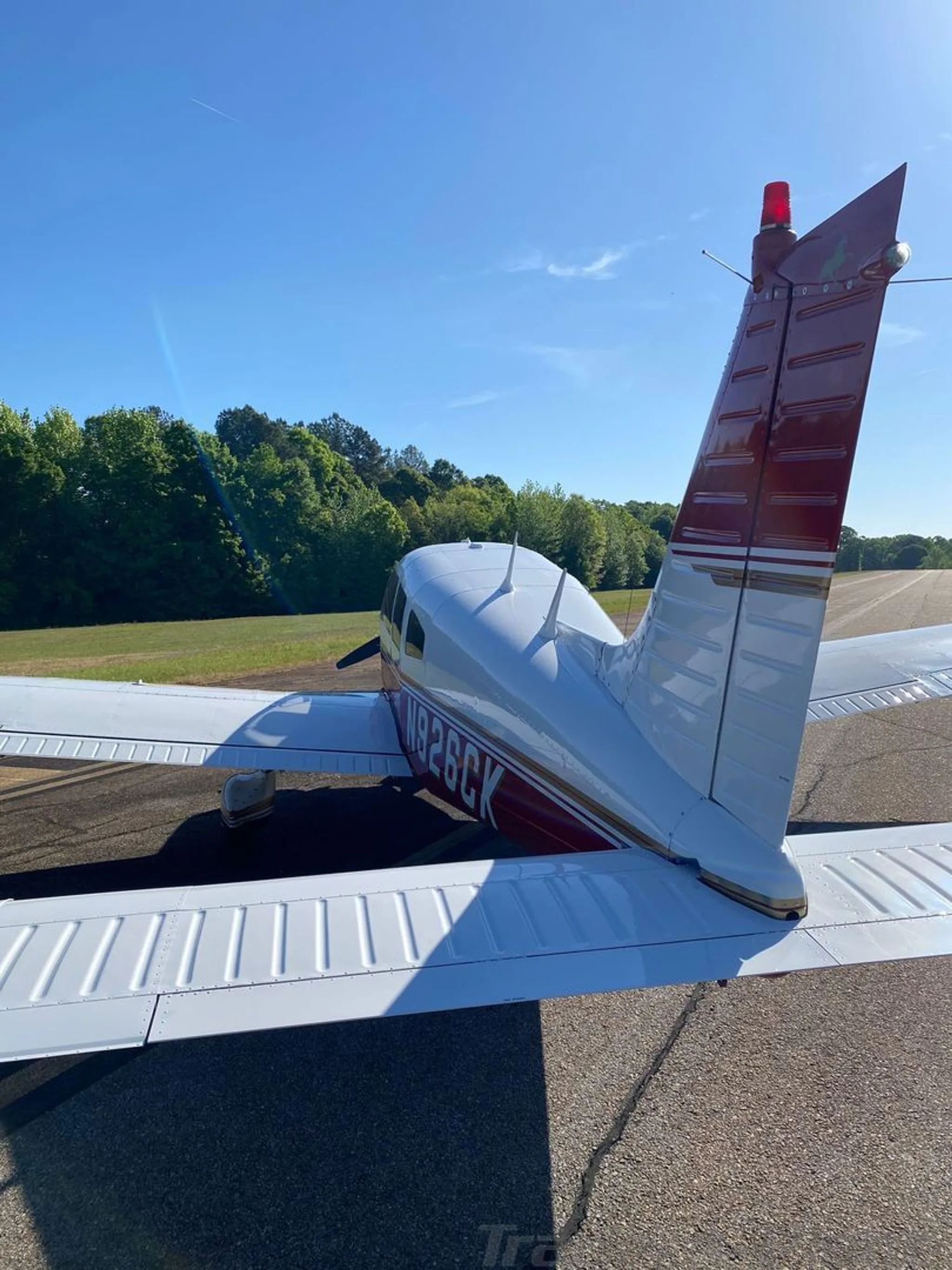 A rear view of the white and red Piper Arrow II (N926CK) showing the tail and right wing on the tarmac.