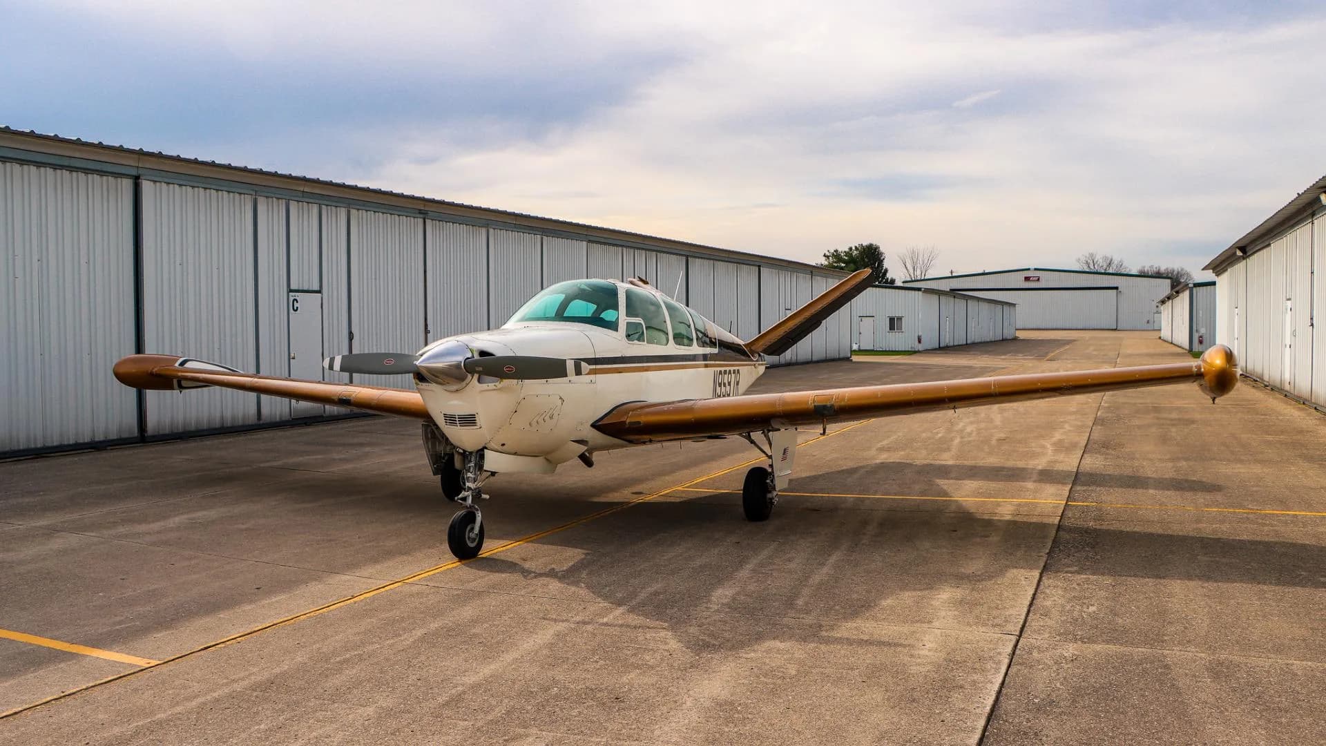 Front three-quarter view of a white and gold Beechcraft Bonanza with tail number N9597R visible.