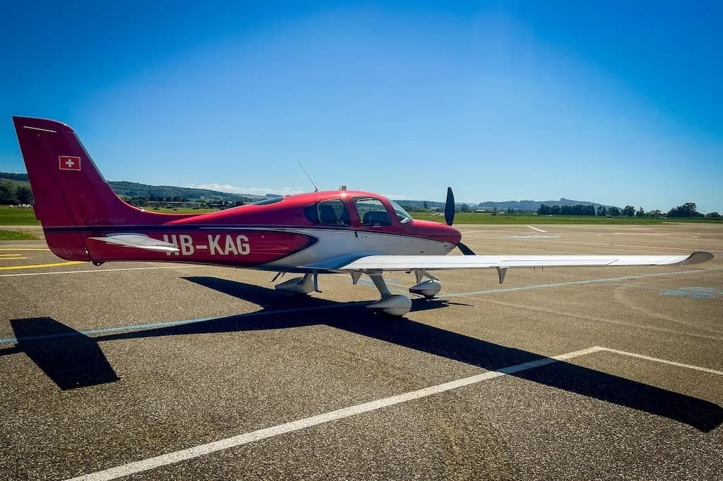 Rear three-quarter view of a red and silver Cirrus SR22 aircraft parked on an airfield.