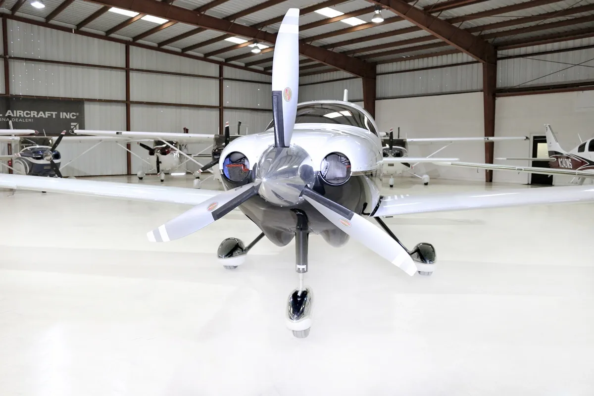 A front view of the white and black single-engine aircraft with its propeller, parked in a hangar.