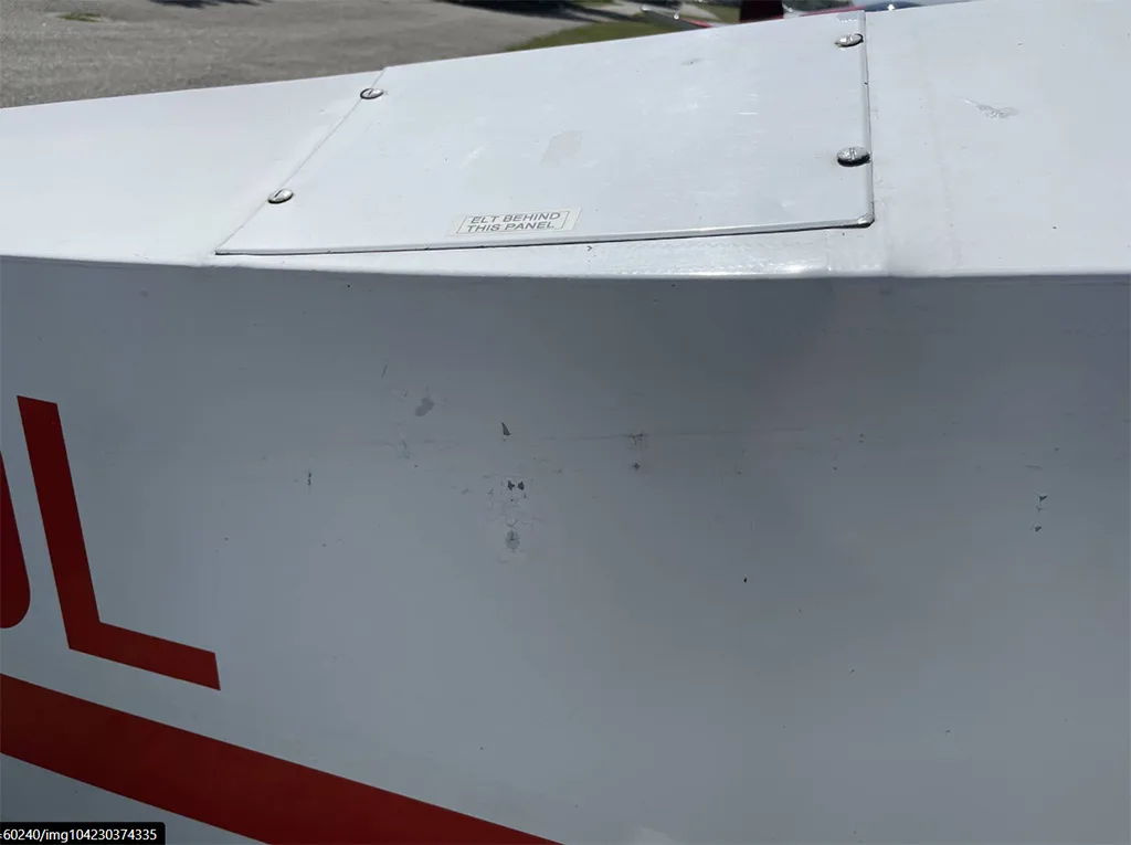 A close-up of a white aircraft fuselage panel with a small "ELT BEHIND THIS PANEL" sticker.