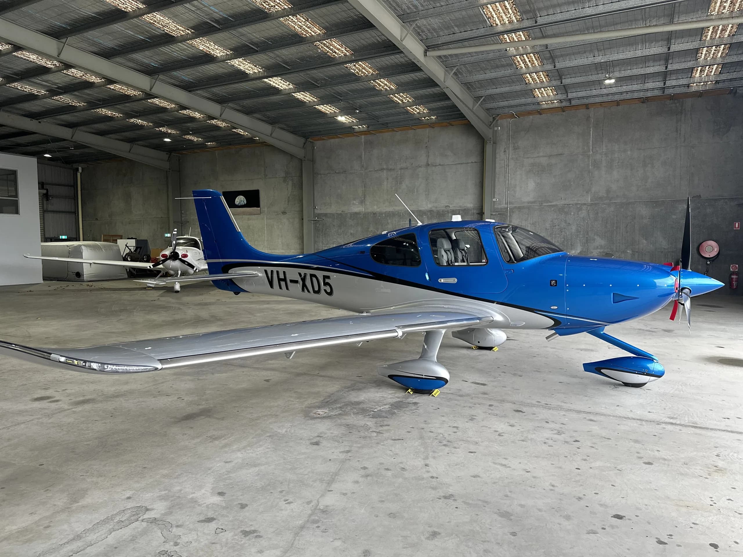 A blue and white single-engine Cirrus SR22 aircraft with registration VH-XD5 parked inside a hangar.