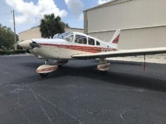 A Piper PA-28-181 Archer II aircraft with a white and red paint scheme parked on the tarmac.