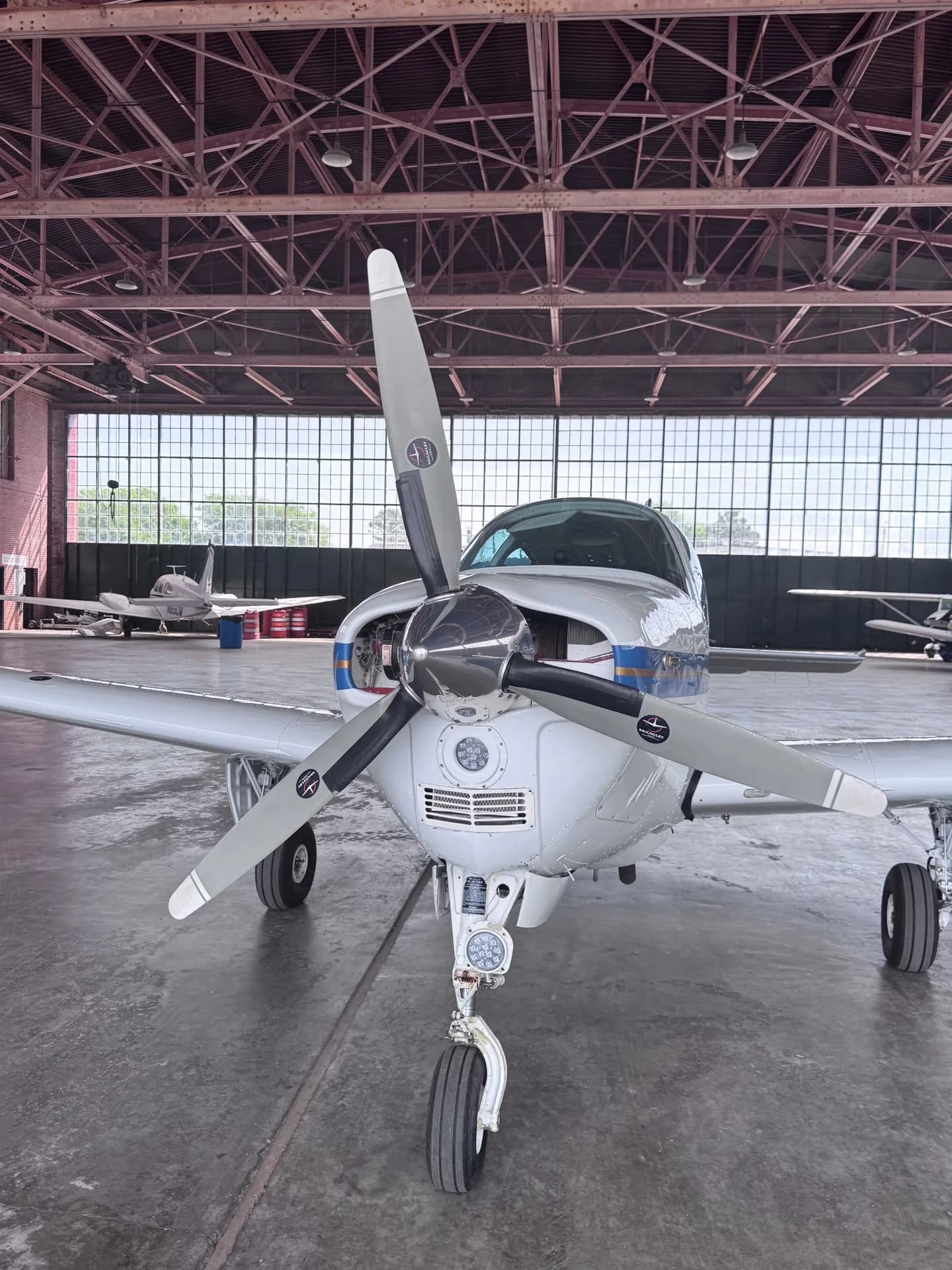 A front view of the white and blue aircraft, highlighting its propeller and nose landing gear, inside a hangar.