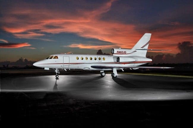 A Falcon 2000 aircraft with registration N463JD is parked on the tarmac at sunset.