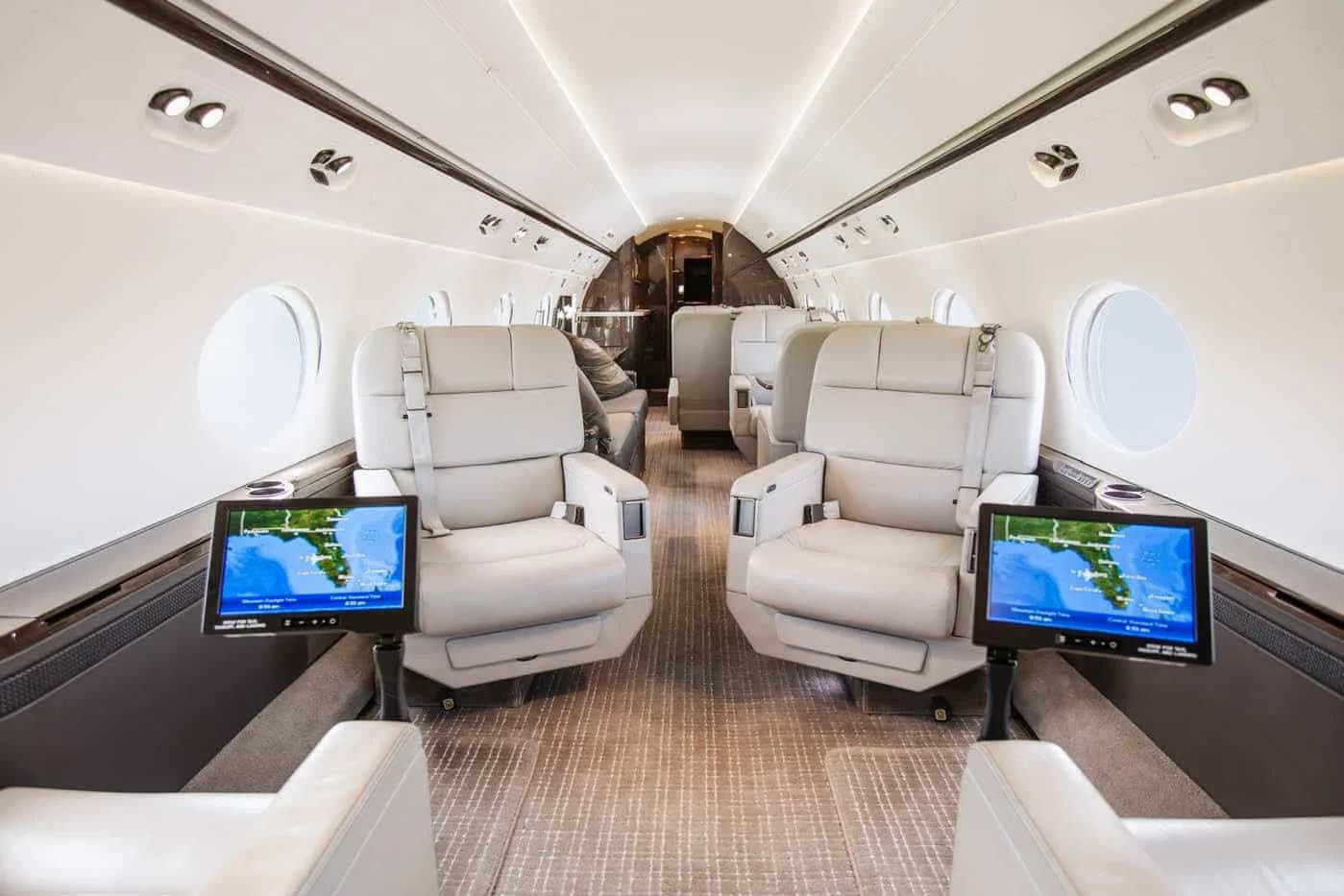 A spacious aircraft cabin with light-colored leather seats and screens showing a map display.
